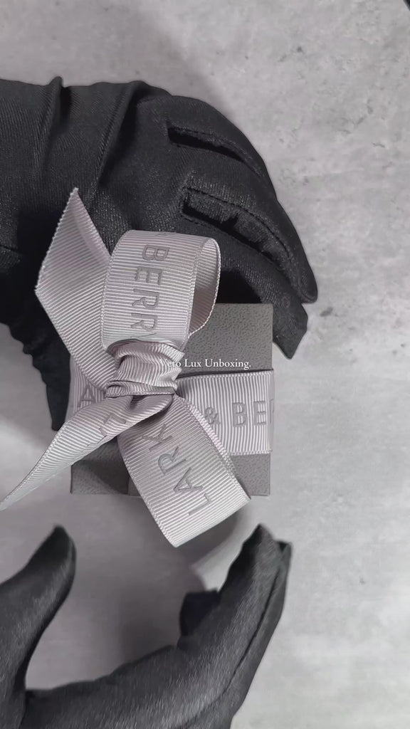 Hands unbox a luxurious Veto Lux diamond stud, revealing a sparkling lab-grown diamond in an elegant jewellery box, set against a soft, grey neutral background.